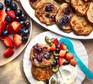 Plate of baby pancakes, yogurt and berries next to a bowl of berries and platter of pancakes