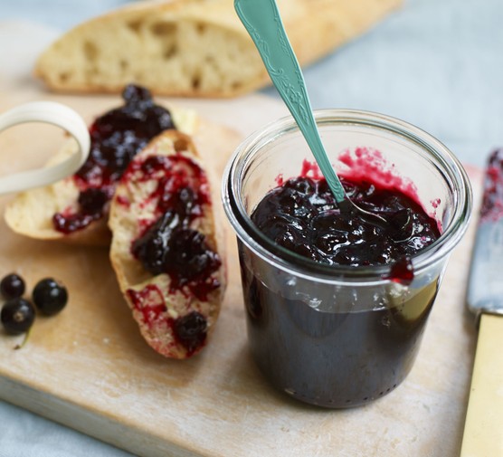Blackcurrant jam in a glass jar with a turquoise spoon and slice of toast