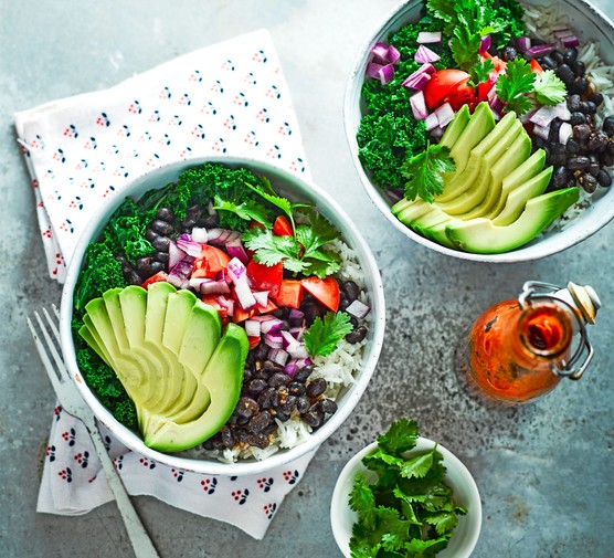 Two burrito bowls with rice, beans, avocado and kale