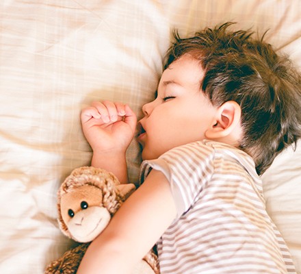 A toddler sleeping with a toy monkey