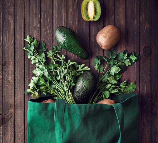 Eco-friendly bag with avocado, kiwi and greenery on wooden background
