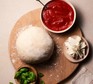 Quick pizza dough Pizza dough on a board next to a bowl of tomato sauce and a ramekin of basil