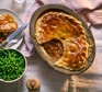 Beef pie with a serving removed next to a bowl of peas