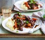 Beef stew with vegetables on mashed potato on plate with fork