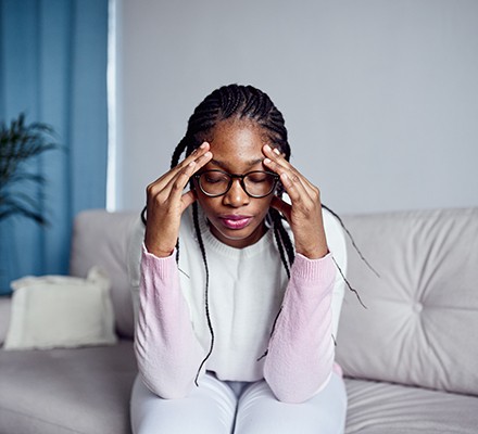 A woman sitting on the sofa with her hands touching her forehead