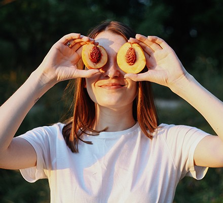 A teenage girl holding peaches in front of her eyes