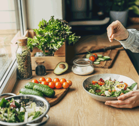 Person cooking on a wooden work surface with tomatoes and green vegetables